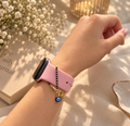 Pink-strap watch with black-bead watch charms, alphabet initial and blue evil eye charm worn on wrist